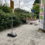 Ein Fußweg ist gesperrt. Eine rot-weiße Absperrung mit gelben Lampen blockiert den Weg. Dahinter steht ein Schild: „Gehweg endet in 30 m“. Links zeigt ein gelbes Schild mit Pfeil nach links: Fußgänger sollen hier abbiegen.
